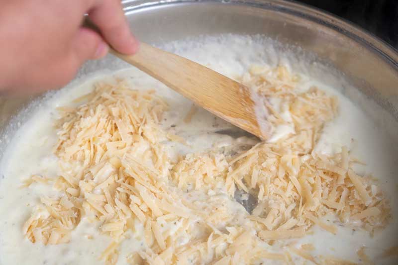 stirring shredded parmesan cheese into homemade alfredo sauce