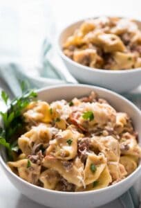 sausage tortellini in white bowls with fresh parsley