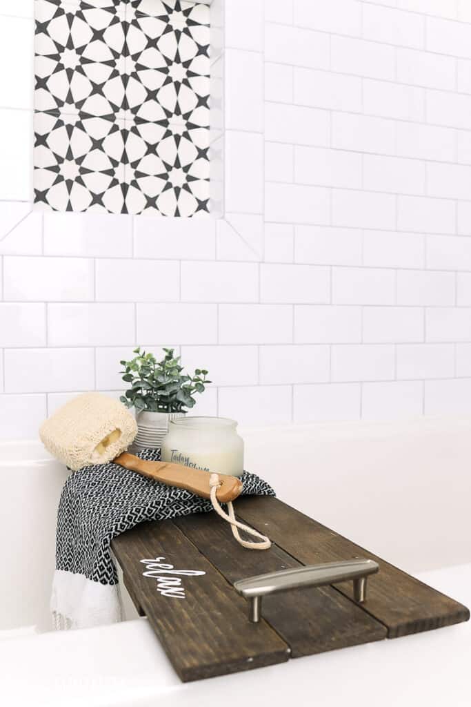 Bath tub with subway tile on the wall and a wood bath tray with loofah and small plant