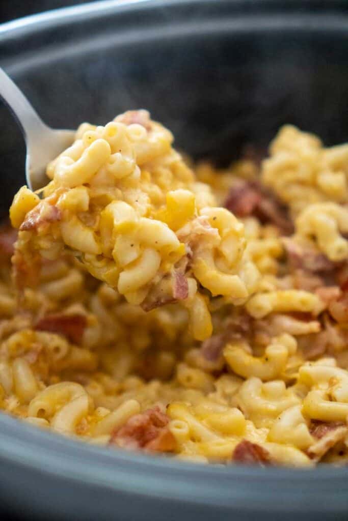 crock pot bacon mac and cheese in spoon over slow cooker