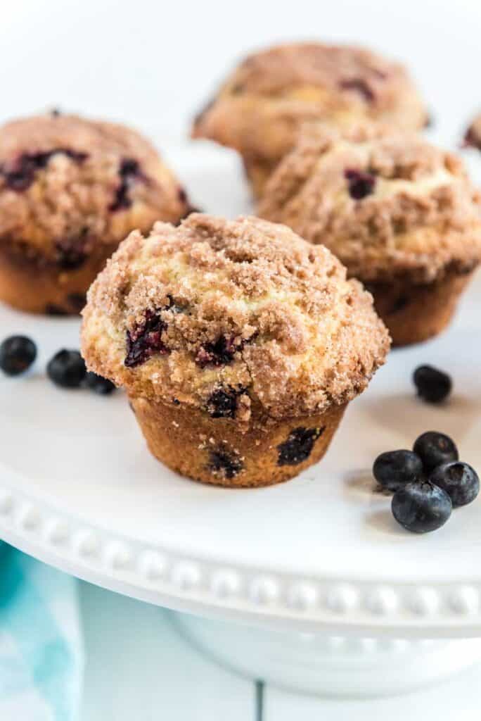 blueberry muffin with streusel topping on white platter with blueberries
