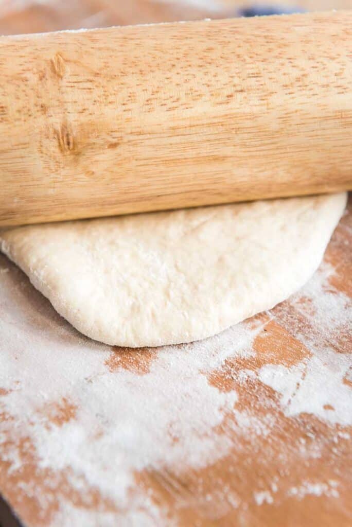rolling naan dough with wooden rolling pin