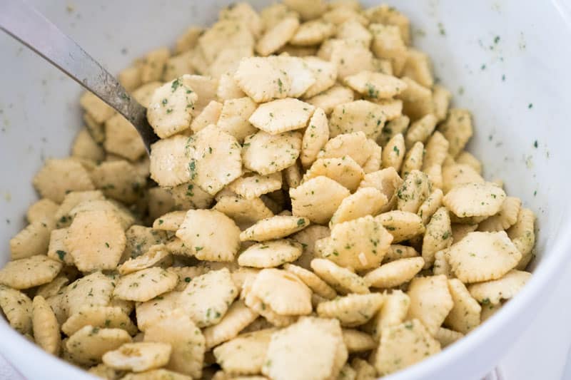 close up of Ranch seasoned oyster crackers in white bowl being scooped up with a large spoon