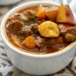 close up of instant pot beef stew in white bowl with brown patterned napkin