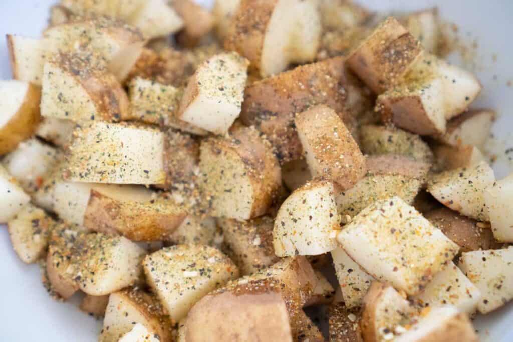 close photo of raw potato cut into 1 inch pieces covered in herb mixture