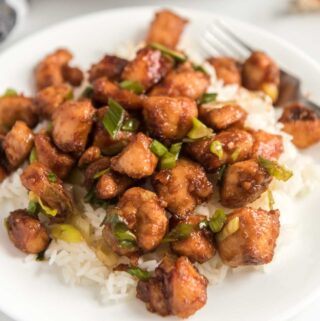 szechuan chicken over rice on white plate with green onion