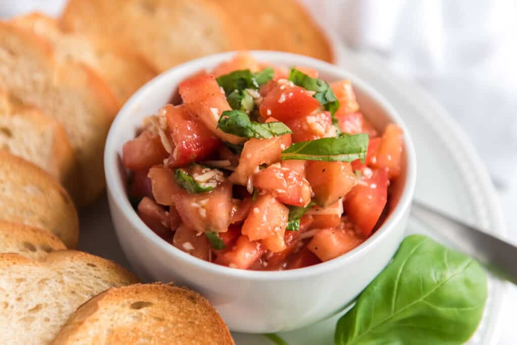 bruschetta in white bowl with slices of toasted bread