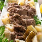 leg of lamb on white platter with potatoes garnished with oregano