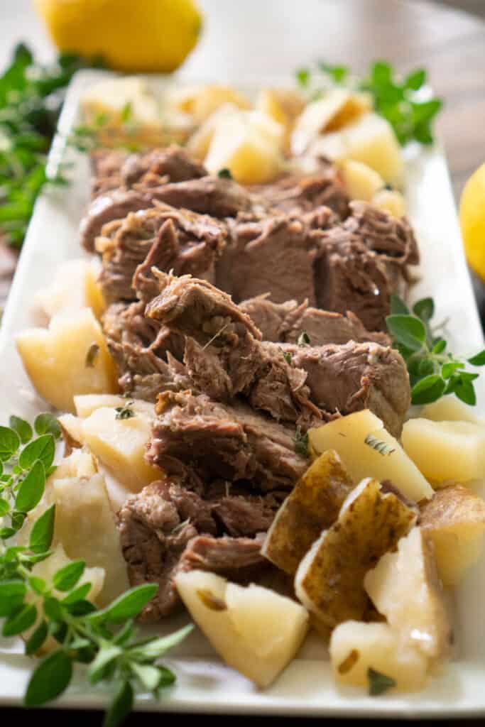 leg of lamb on white platter with potatoes