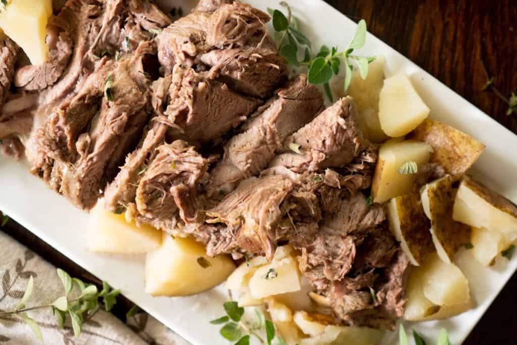 greek leg of lamb on white platter with potatoes