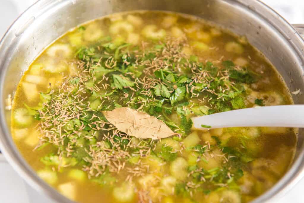 vegetable soup in a large pot with white spoon stirring in herbs