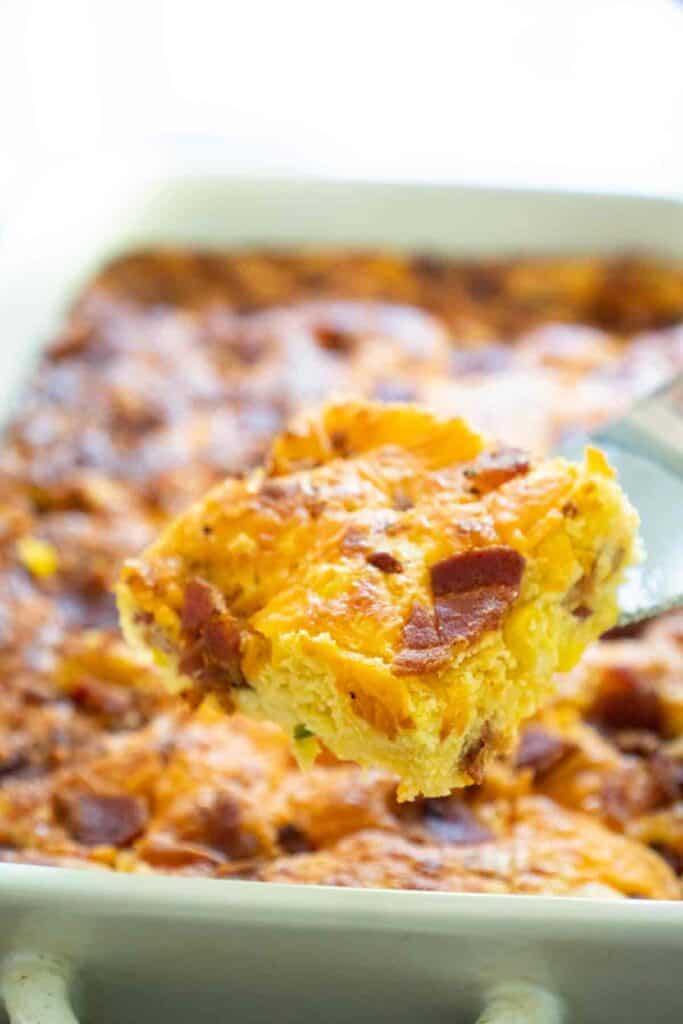 piece of bacon jalapeño cheddar cornbread on spatula over entire loaf in the background