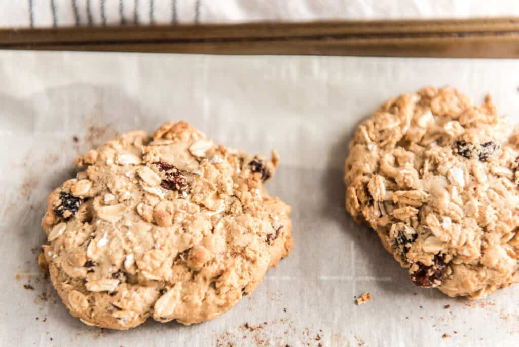 two oatmeal raisin cookies on a baking sheet lined with parchment paper