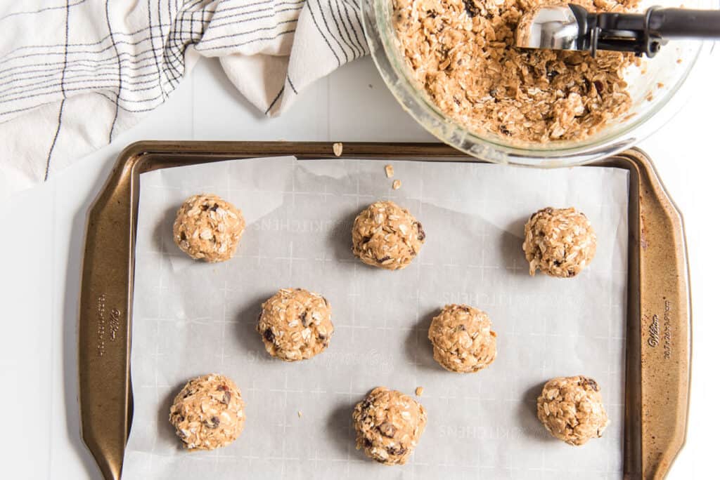 oatmeal raisin cookie dough rolled into balls on baking sheet lined with parchment paper before baking