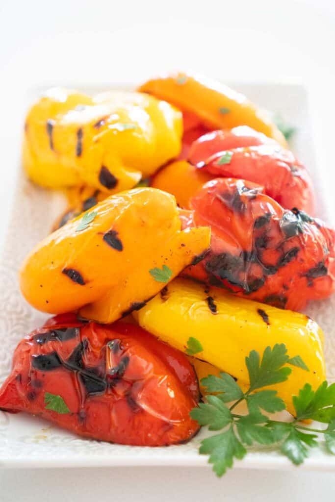 grilled bell peppers on white serving platter with parsley