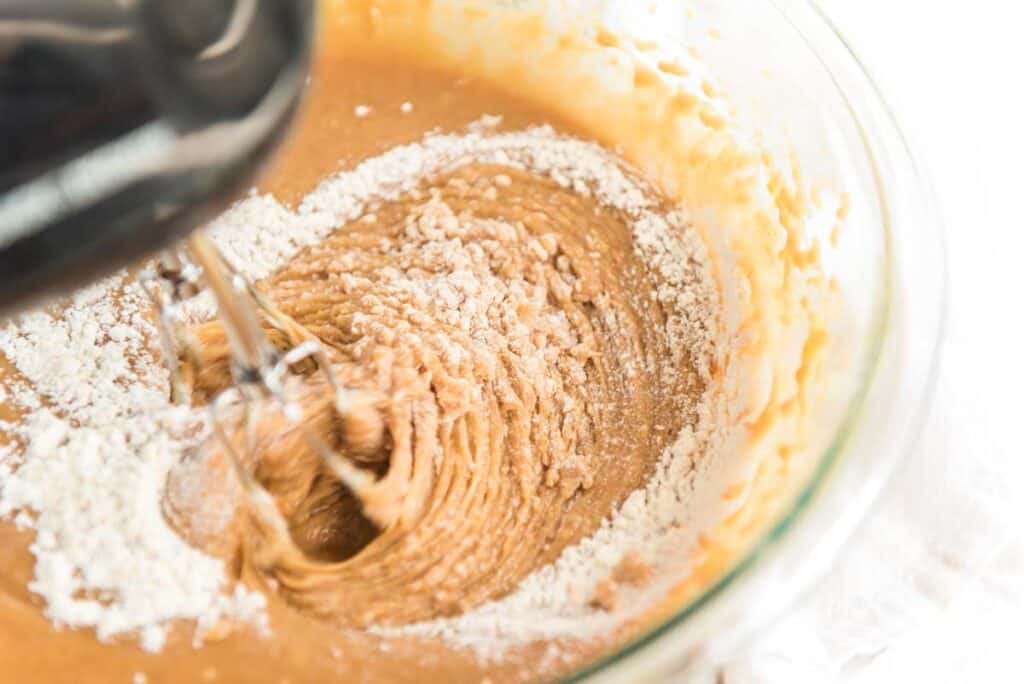 beating flour into peanut butter cupcake batter in glass bowl with hand mixer
