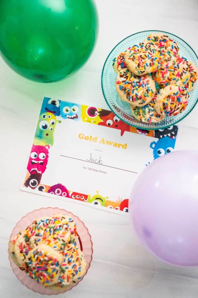 overhead view of award certificate with green and purple balloons and two cake stands with cookies on them