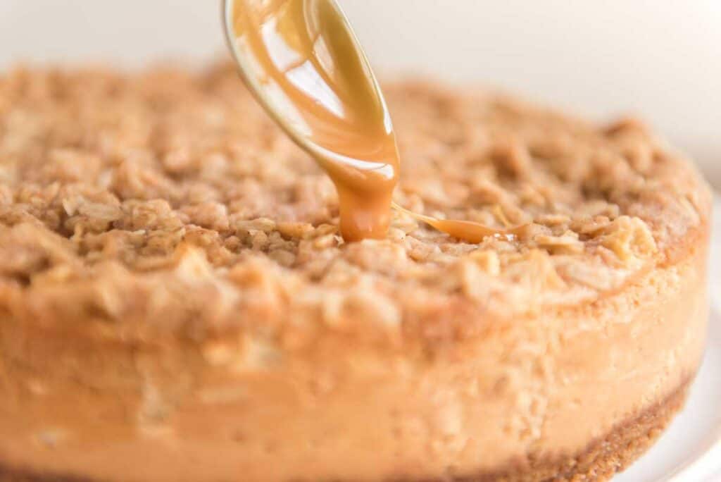spoon drizzling caramel over apple crisp cheesecake
