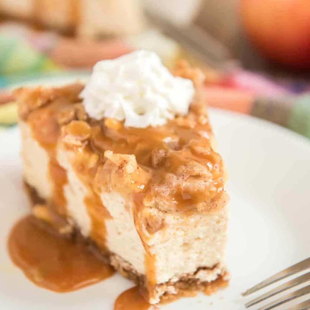 slice of apple crisp cheesecake on white plate with bite taken out