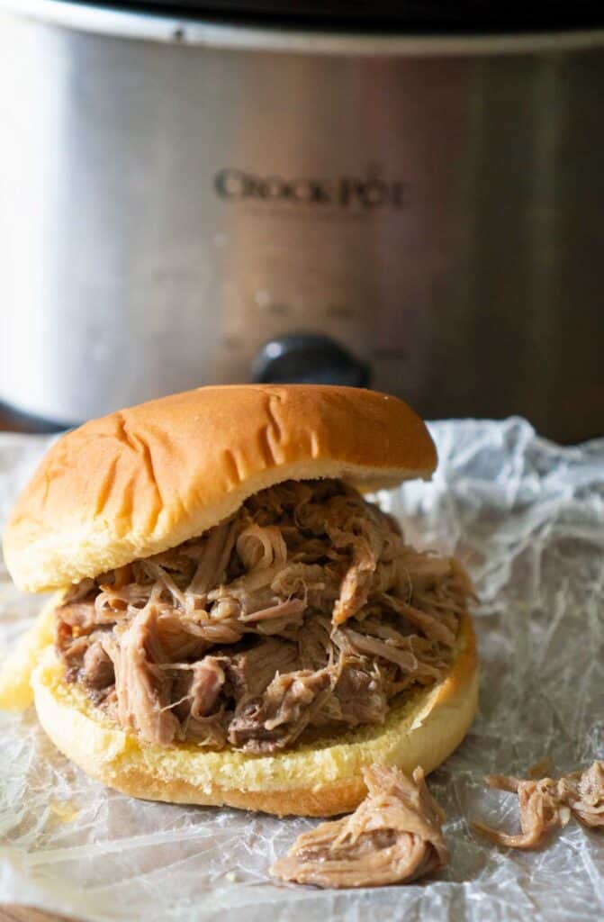 pulled pork sandwich on crumpled wax paper with slow cooker in the background