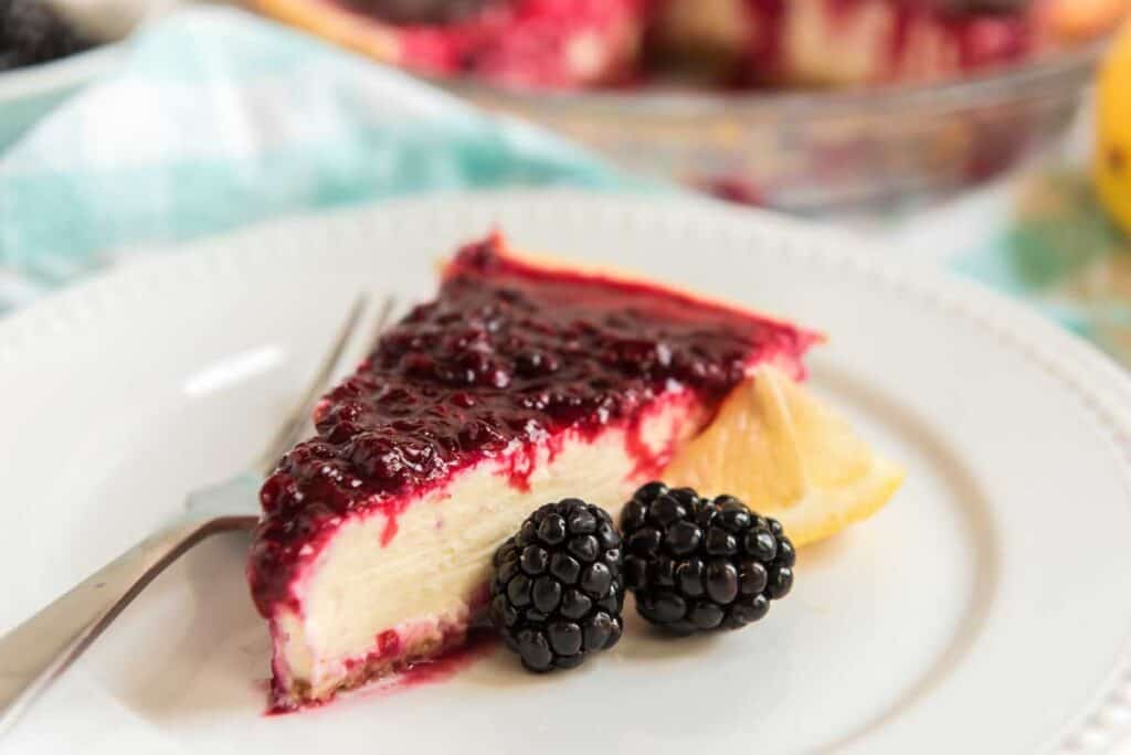 piece of lemon cheesecake with blackberry sauce on white plate