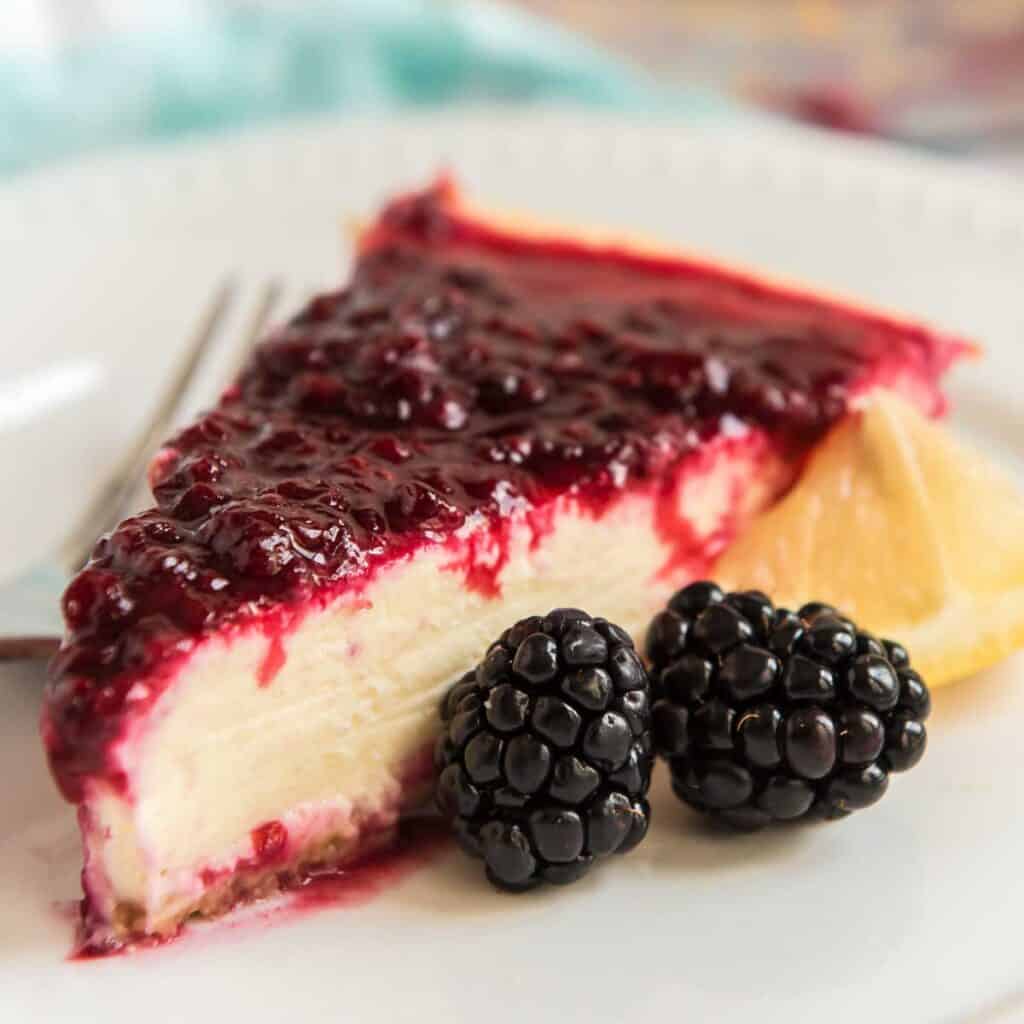 side view of lemon cheesecake with blackberry sauce on white plate