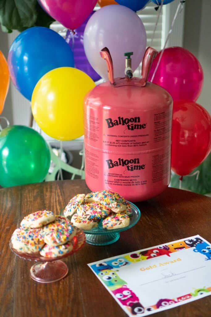 wood table with helium tank, cookies on cake stands and balloons in background