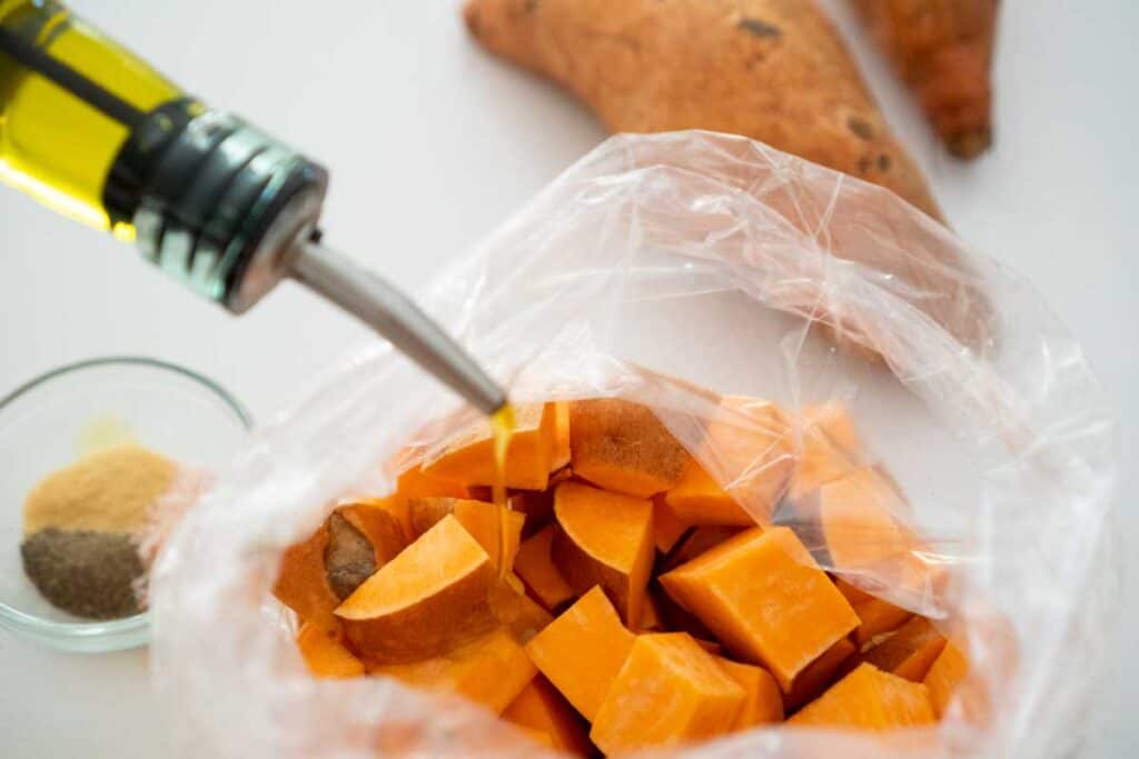 Adding olive oil to bag of sweet potato cubes