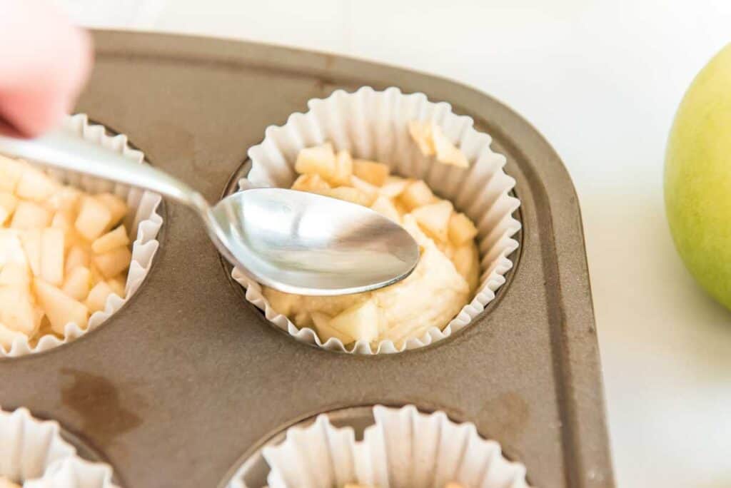spoon patting diced apple into muffin batter in tin