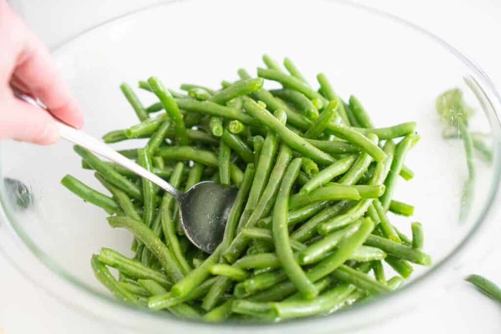 spoon stirring green beans in glass bowl