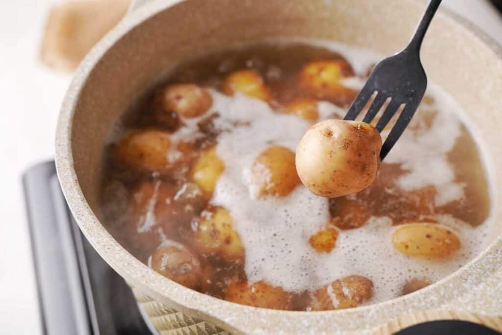 fork holding a baby potato over a pot of boiling water