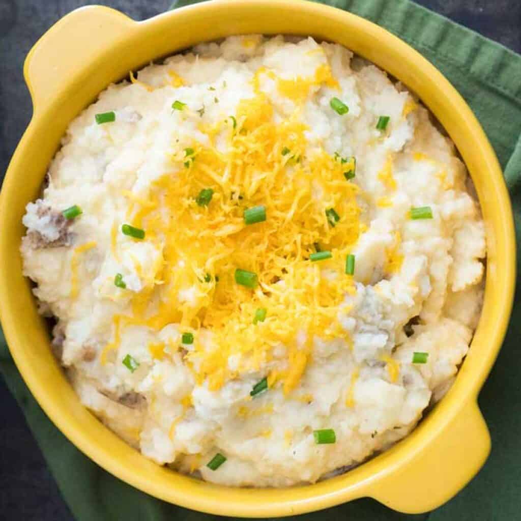 overhead view of yellow bowl with mashed potatoes topped with cheese and green onion