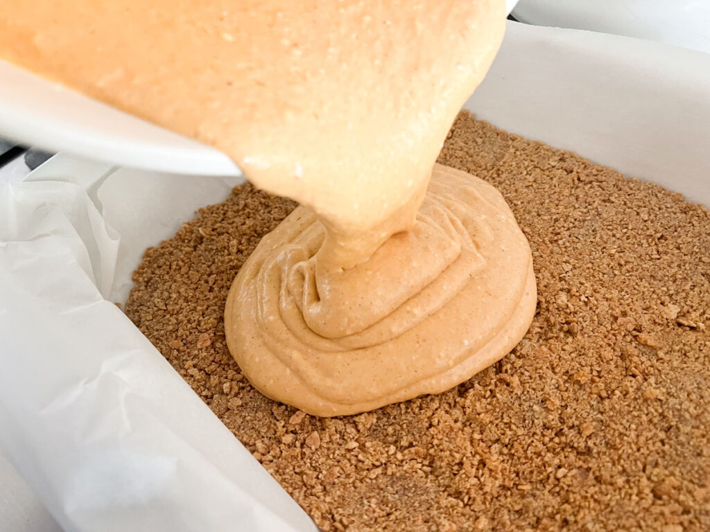 pouring pumpkin cheesecake filling over graham cracker crust