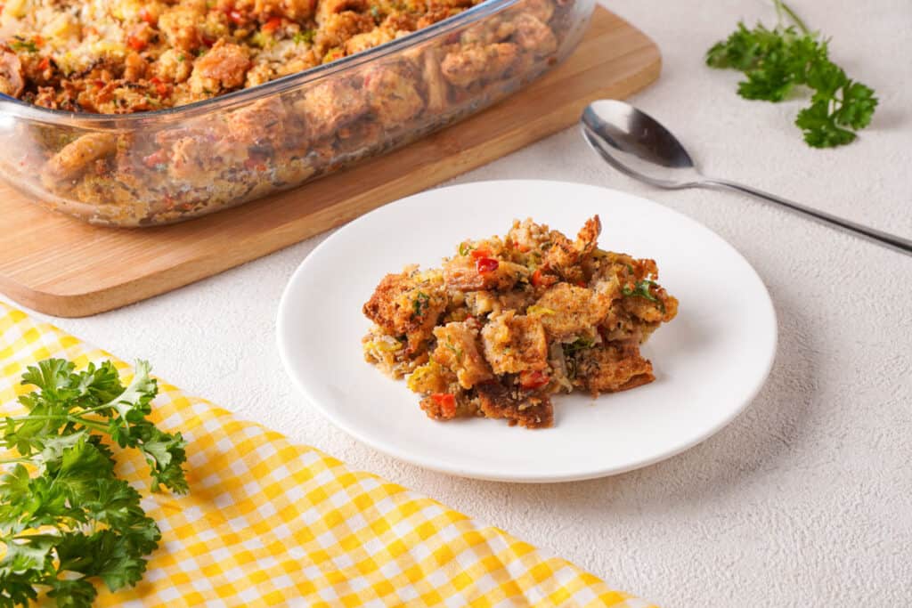 sausage and herb stuffing on white plate with baking dish and spoon in background