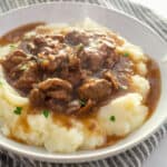 beef tips and gravy over mashed potatoes in white bowl