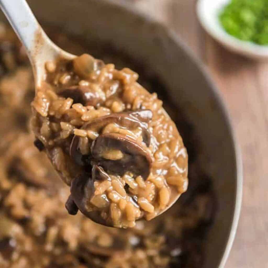 spoon with mushroom risotto held over pan of risotto