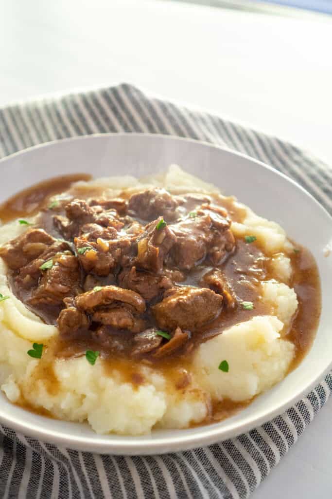 beef tips over mashed potatoes in white bowl
