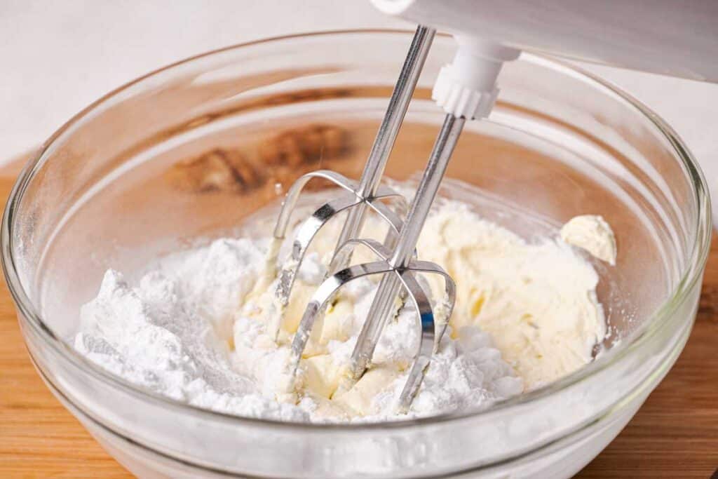 mixer mixing cream cheese frosting in a glass bowl
