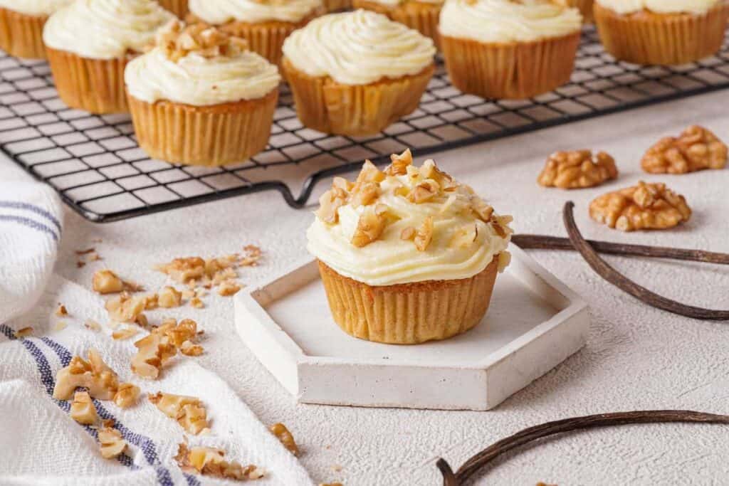 carrot cake muffin topped with cream cheese frosting and chopped walnuts with more muffins in background