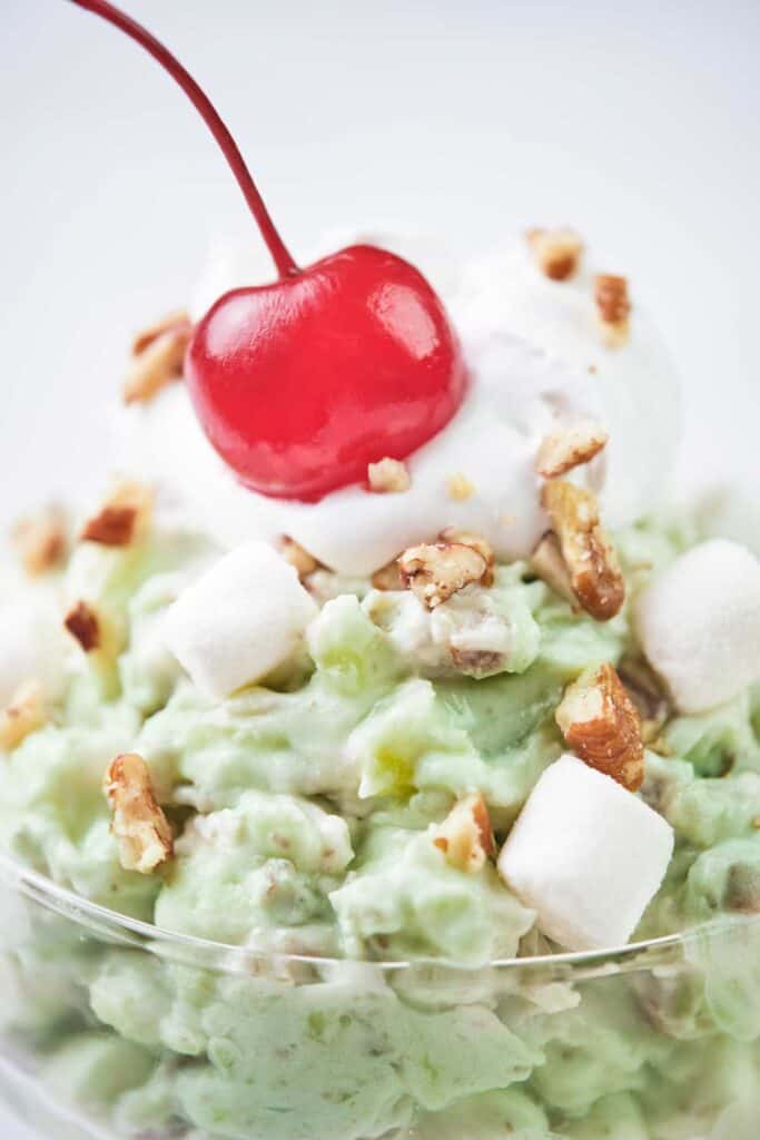 close up of watergate salad topped with chopped pecans and a maraschino cherry