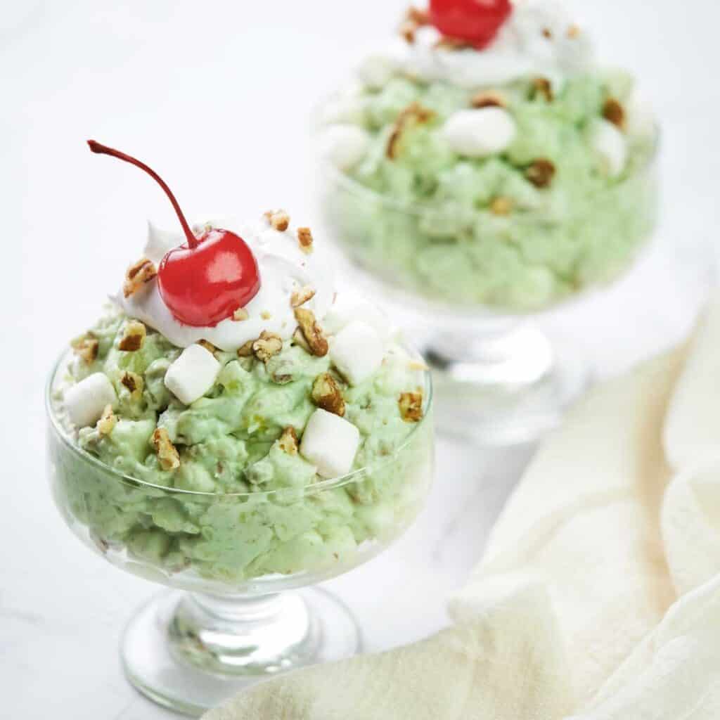 two glass dishes of watergate salad topped with cherries