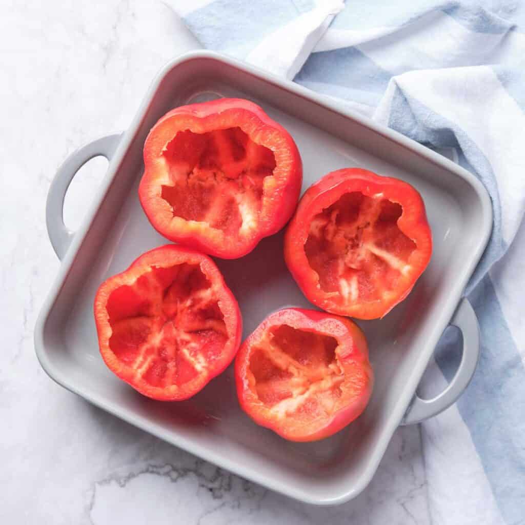 four red bell peppers with tops removed in baking dish