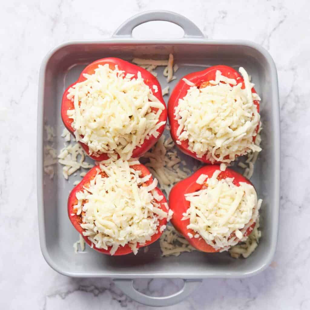 four red stuffed peppers topped with cheese in baking dish