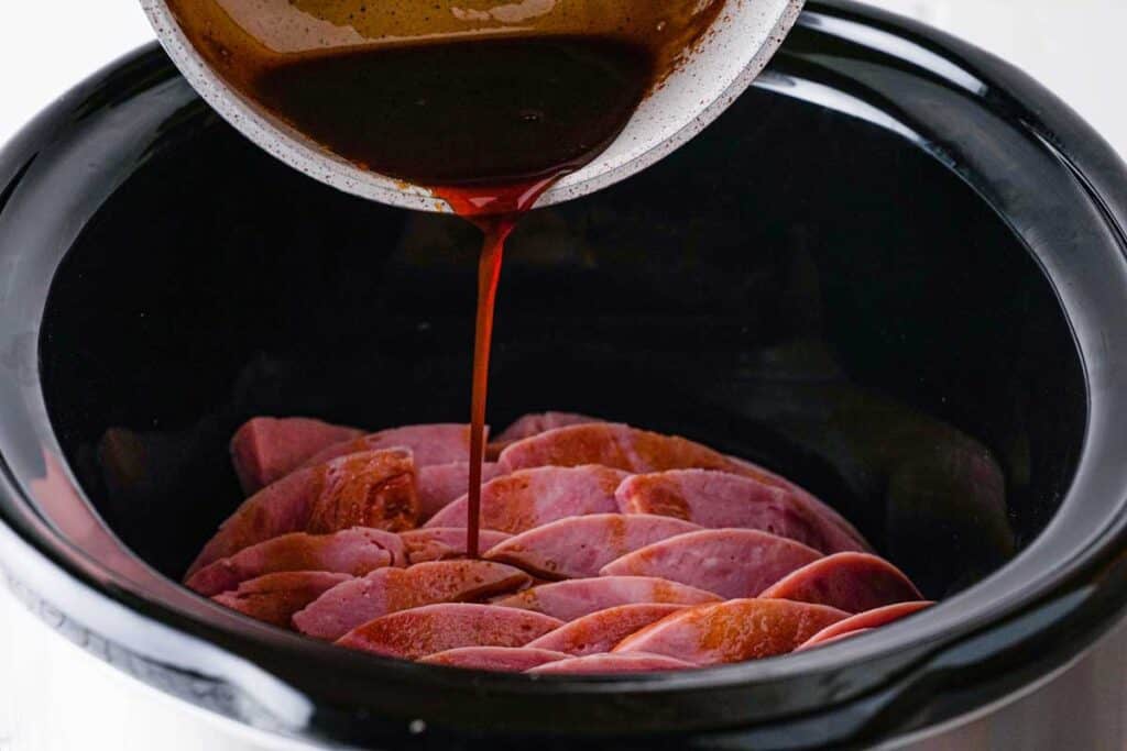 pouring glaze over sliced ham in slow cooker