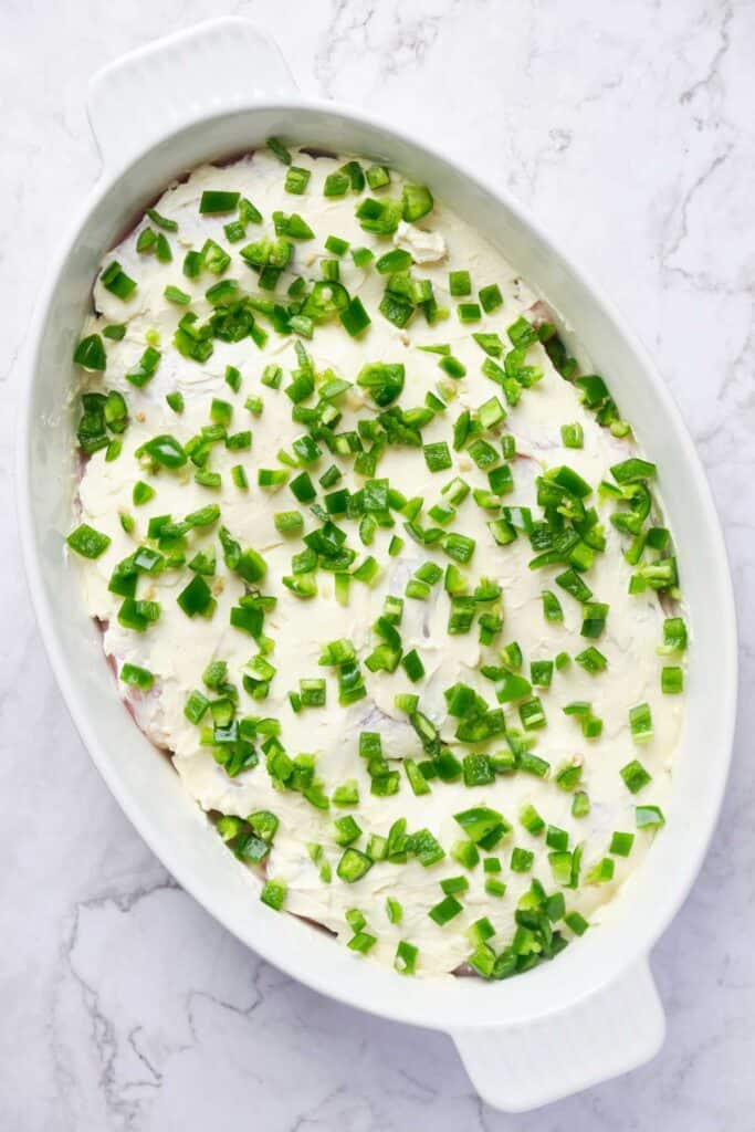 chicken in baking dish topped with cream cheese and chopped jalapeños