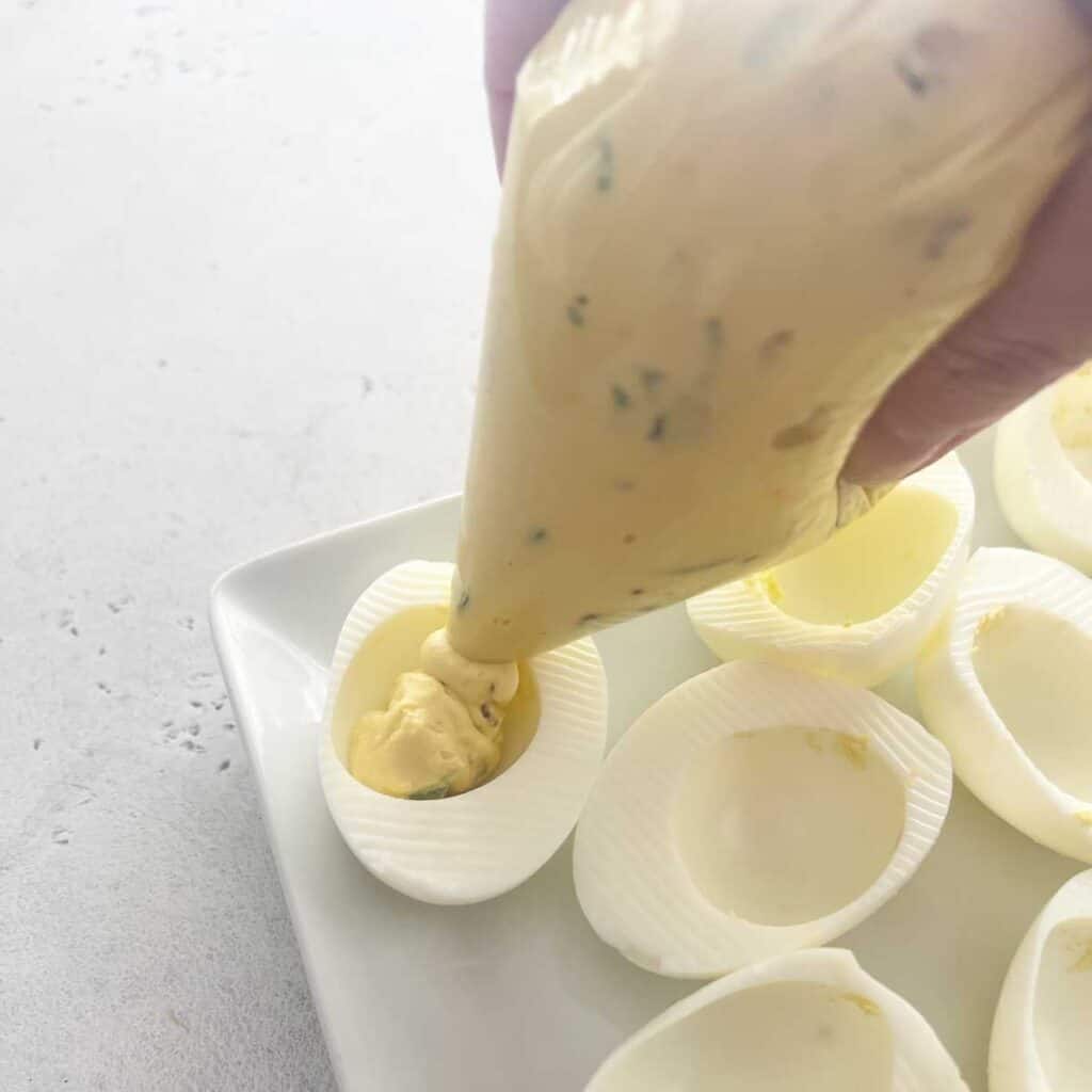 piping egg yolk mixture into deviled egg with sandwich bag