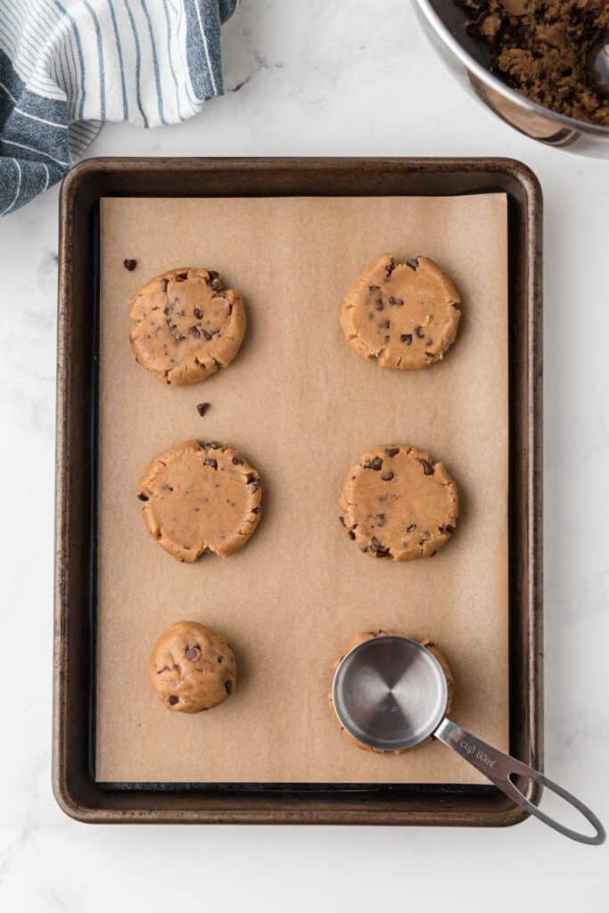 cookie dough balls being squished on baking sheet