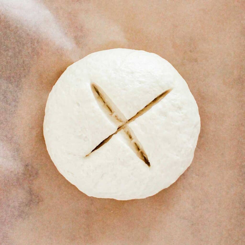 Irish soda bread dough ball with cross cur in it on parchment paper