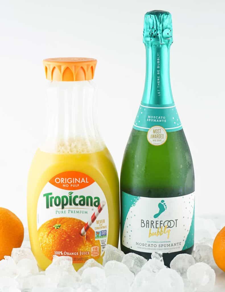 champagne bottle and orange juice bottle with ice cubes and oranges
