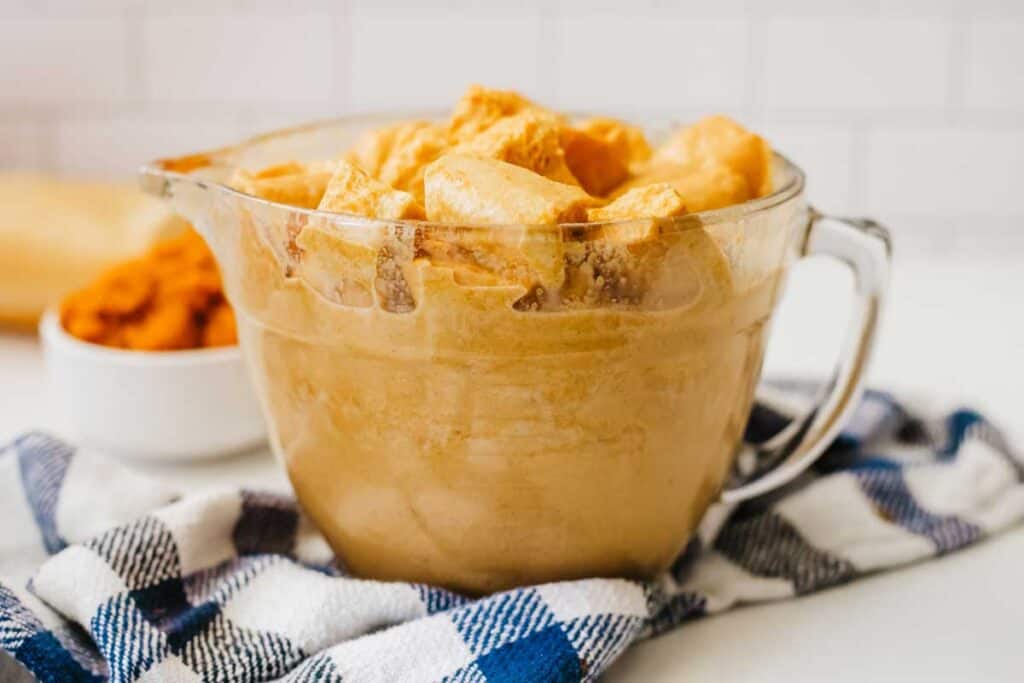 glass measuring cup with bread pudding cubes soaked in pumpkin spice custard mixture